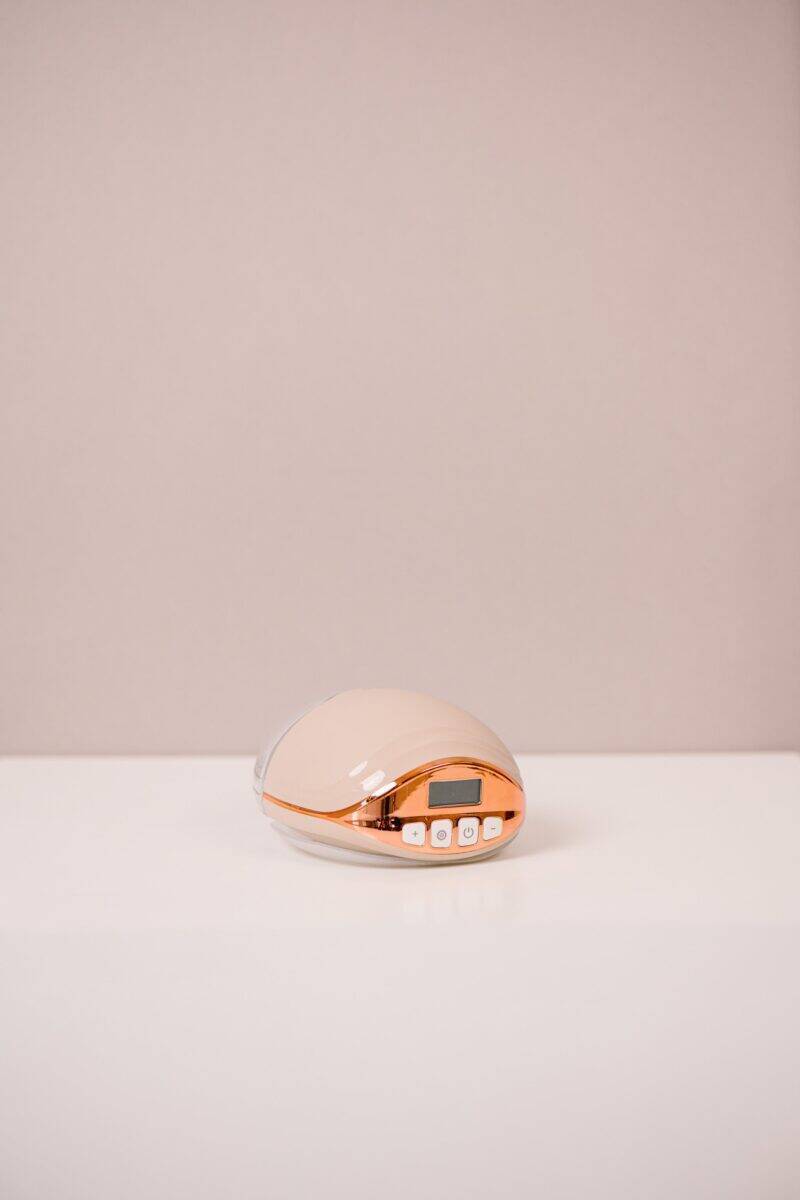 Difrax Handsfree Breastpump in soft pink with rose gold accents, featuring a digital display and control buttons.
