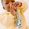 Difrax Crown Teething Ring in use by a baby wearing a yellow sweatshirt, holding the ring close to their mouth.