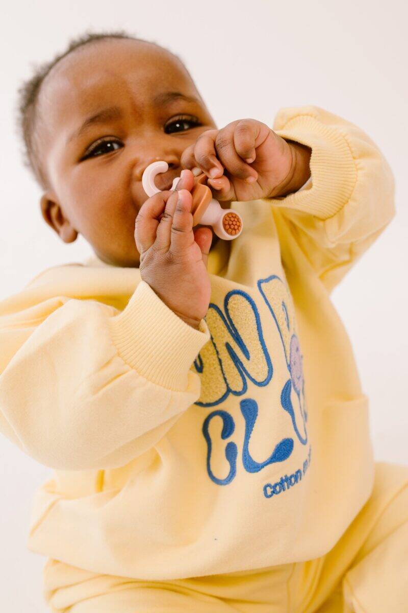 Difrax Crown Teething Ring in use by a baby wearing a yellow sweatshirt, holding the ring close to their mouth.