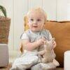 Love to Dream Swaddle Up Sleep Suit in Daydream Grey, featuring a baby sitting with a toy in a cozy setting.