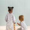 Love To Dream Sleep Suit Long Sleeve 1.0 Tog in white with animal print, featuring two children playing with a wooden toy.