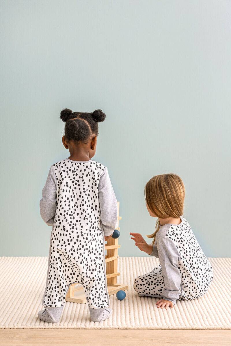 Love To Dream Sleep Suit Long Sleeve 1.0 Tog in white with animal print, featuring two children playing with a wooden toy.