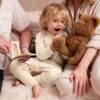 Love to Dream Sleep Suit Long Sleeve 2.5 TOG in Oatmeal Bees, child smiling while holding a teddy bear with family.