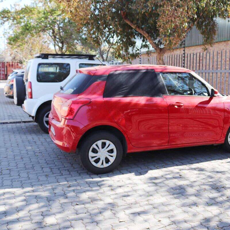 Snuggletime Curved Window Shades on a red car parked in a sunny lot, providing shade and privacy for the vehicle.