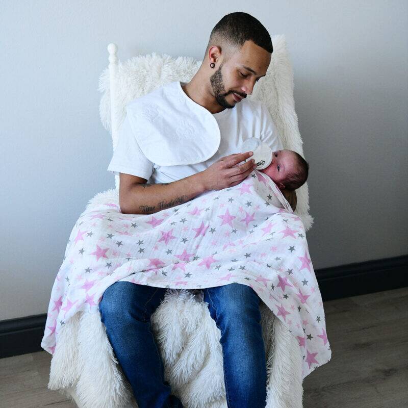 Snuggletime Deluxe Muslin Receiver in pink with star patterns, wrapped around a baby during feeding in a cozy setting.