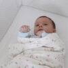Snuggletime Deluxe Muslin Receiver in pink blossoms, wrapped around a baby lying on a white crib mattress.
