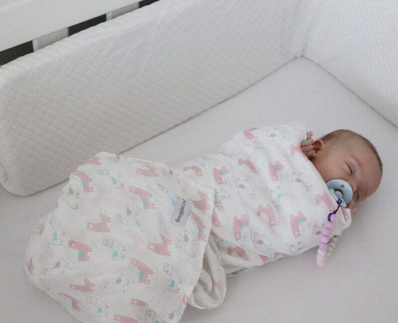 Snuggletime Bamboopaedic Cot Bumper and Cover in a nursery, featuring a sleeping baby wrapped in a soft, patterned blanket.