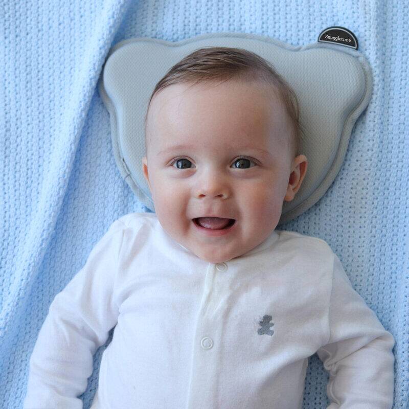 Snuggletime 3D Flat Head Baby Pillow in gray, supporting a smiling baby on a soft blue blanket.