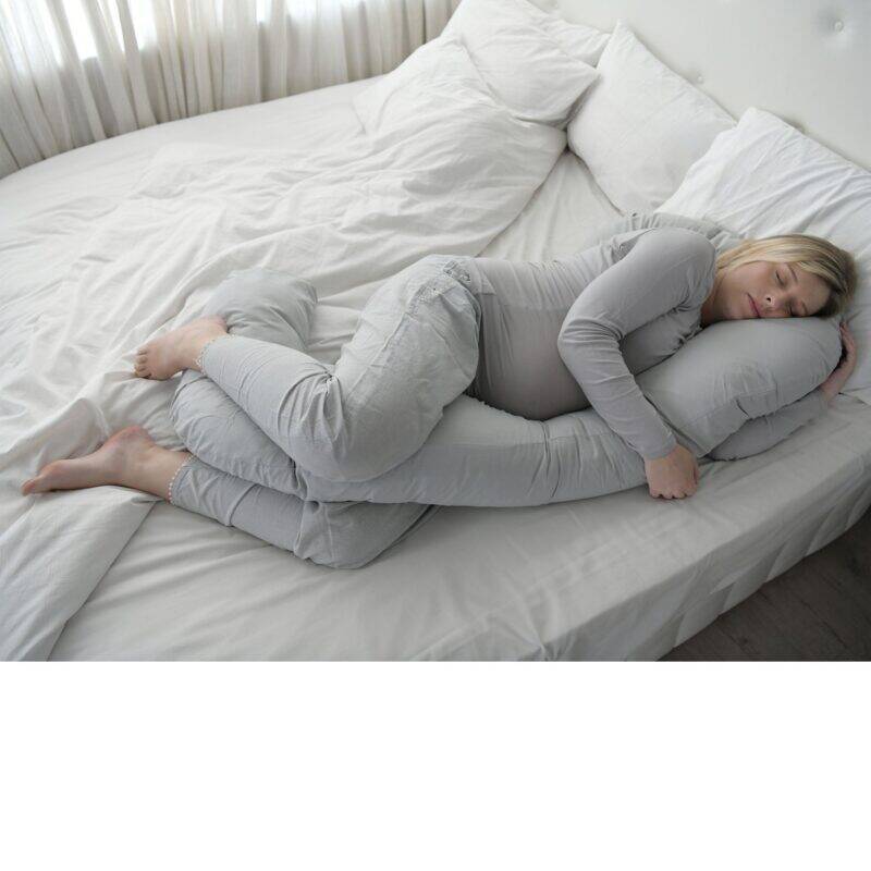 Snuggletime Body Comfort Pillow in grey, designed for support and comfort, shown in a cozy bedroom setting with a woman