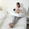 Snuggletime Body Comfort Pillow in white, supporting a mother cradling her baby while sitting on a bed.