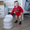 Snuggletime Comfort Toilet Seat Potty in white, with a toddler wearing a red hoodie, smiling in a nursery setting.