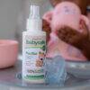 BabySafe Pacifier Cleaner & Sanitiser 100ml with spray nozzle, shown in use while cleaning a pacifier beside a child.