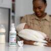 BabySafe Pacifier Cleaner & Sanitiser 100ml on a countertop with a caregiver holding a baby, showcasing a nurturing