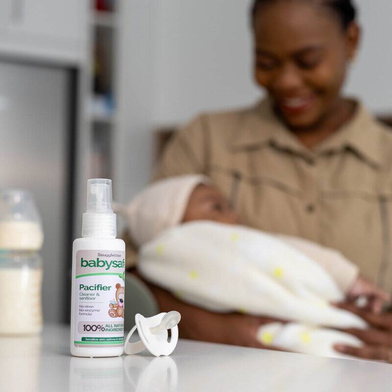 BabySafe Pacifier Cleaner & Sanitiser 100ml on a countertop with a caregiver holding a baby, showcasing a nurturing