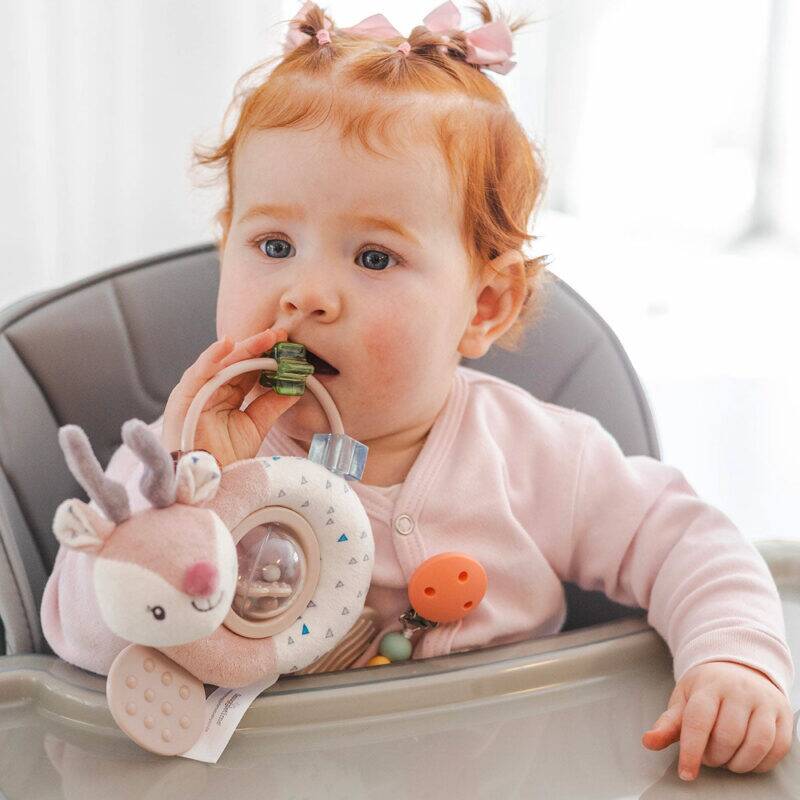 Back To Nature Teether & Spinning Rattle in blue and pink, featuring a cute animal design, held by a baby in a high chair.