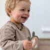 Back To Nature Rabbit Teether Ring in green, held by a smiling toddler, featuring soft ears for easy gripping.