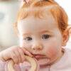 Back To Nature Rabbit Teether Ring in pink, held by a baby with red hair, featuring a wooden ring for soothing gums.