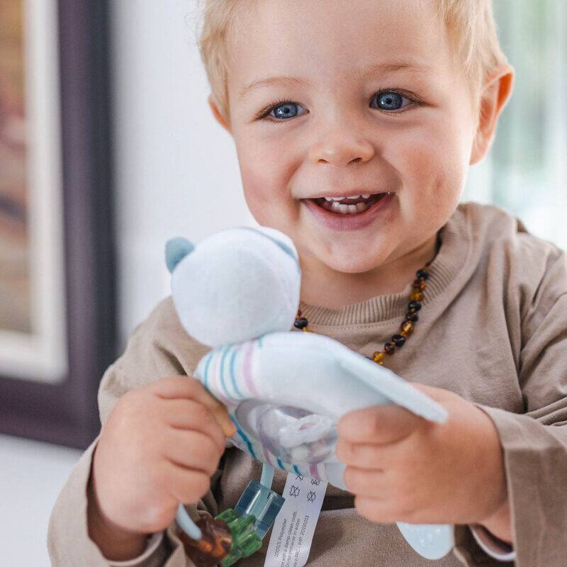 Back To Nature Teether & Spinning Rattle in blue and pink, held by a smiling toddler in a cozy indoor setting.