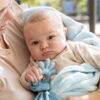 Beige and blue Back To Nature Silicone Teether Muslin Blankie held by a baby in a cozy setting, featuring a soft fabric.