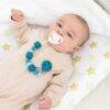 Back To Nature Silicone Pacifier Clip in blue and pink, featuring a cube design, attached to a baby’s pacifier.