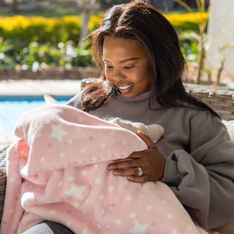 Snuggletime Double Fleece Baby Blanket in pink with white stars, cozy setting outdoors with a woman holding a baby.