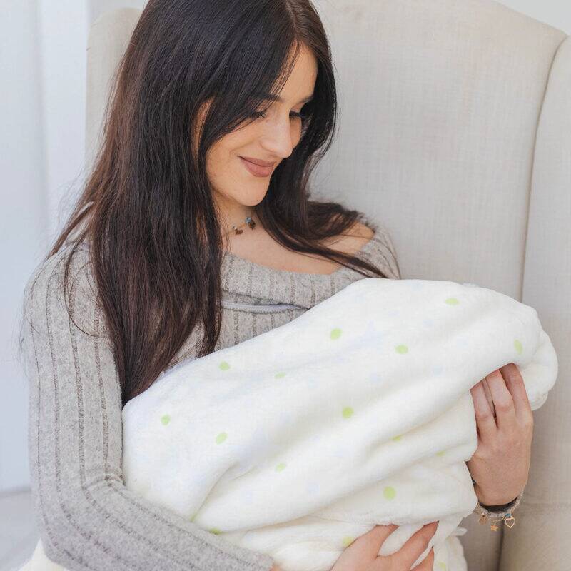 Snuggletime Double Fleece Baby Blanket in cream with green polka dots, held by a woman in a cozy setting.