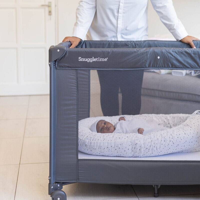 Snuggletime Classic Comfort Camp Cot in gray, featuring a mesh side for visibility, with a baby peacefully resting inside.