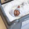 Snuggletime Classic Comfort Camp Cot with a baby in a grey outfit and hat, lying on a star-patterned mattress.