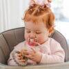 Back to Nature Silicone Teether Leaf in use by a baby with red hair in a high chair, exploring the teether with curiosity.