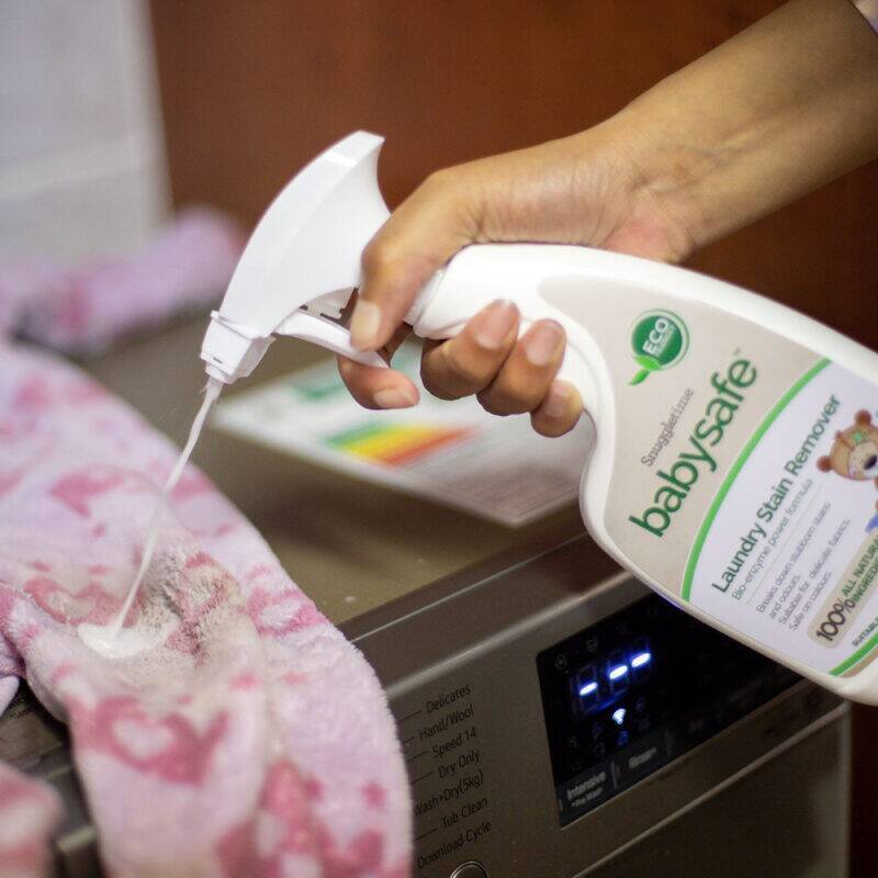 BabySafe Laundry Stain Remover spray bottle being used on a pink towel near a washing machine.