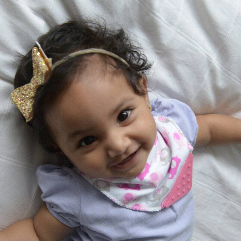 Snuggletime 2-in-1 Teether Bandana Bib in butterfly print worn by a smiling baby on a soft surface.