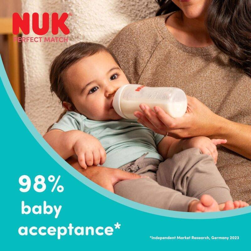 Nuk Perfect Match 120ml glass bottle in rainbow style, held by a caregiver while a baby drinks comfortably.