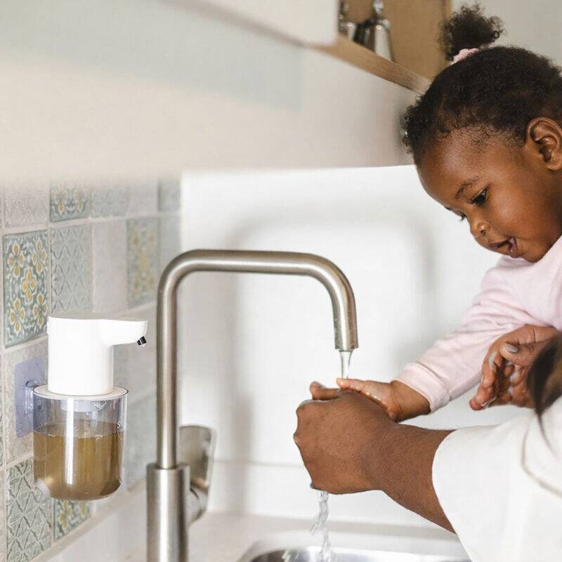 BabySafe Touchless Foam Soap Dispenser mounted in a kitchen, with a child washing hands under a faucet.