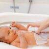 Aromababy baby oil being applied to a newborn during a bath, showcasing gentle skincare in a serene setting.