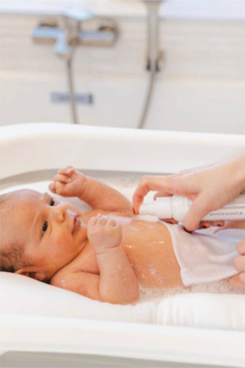 Aromababy baby oil being applied to a newborn during a bath, showcasing gentle skincare in a serene setting.
