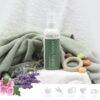 Aromababy baby lotion in a spray bottle on a soft green towel, surrounded by lavender and colorful natural elements.
