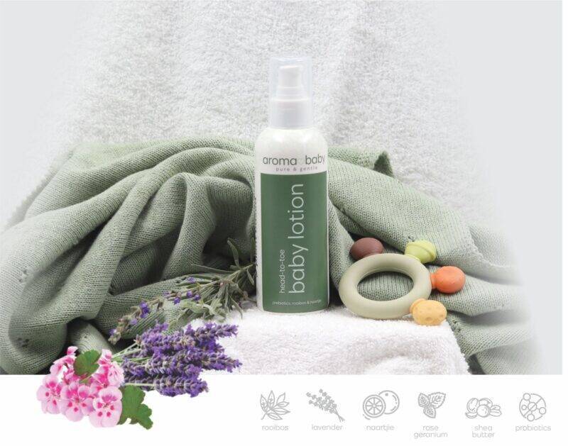 Aromababy baby lotion in a spray bottle on a soft green towel, surrounded by lavender and colorful natural elements.