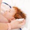 Aromababy Cradle Cap treatment being applied to a baby’s scalp, showcasing the product and the child's curly red hair.