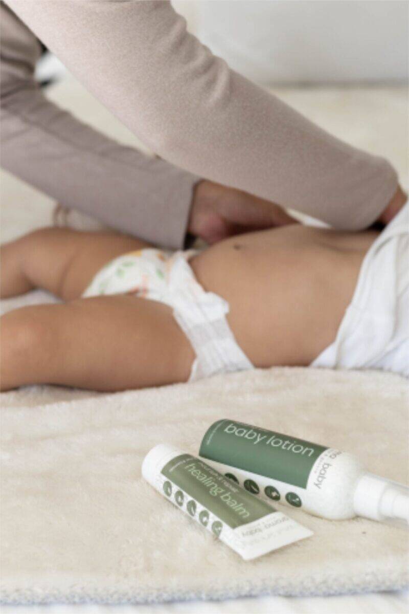 Aromababy Healing Balm and Baby Lotion displayed beside a baby lying on a soft blanket, emphasizing gentle skincare.