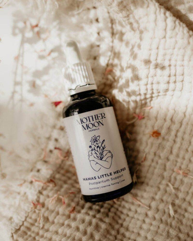 Mother Moon Mama's Little Helper postpartum support tincture in a dark glass bottle with a dropper, placed on a textured