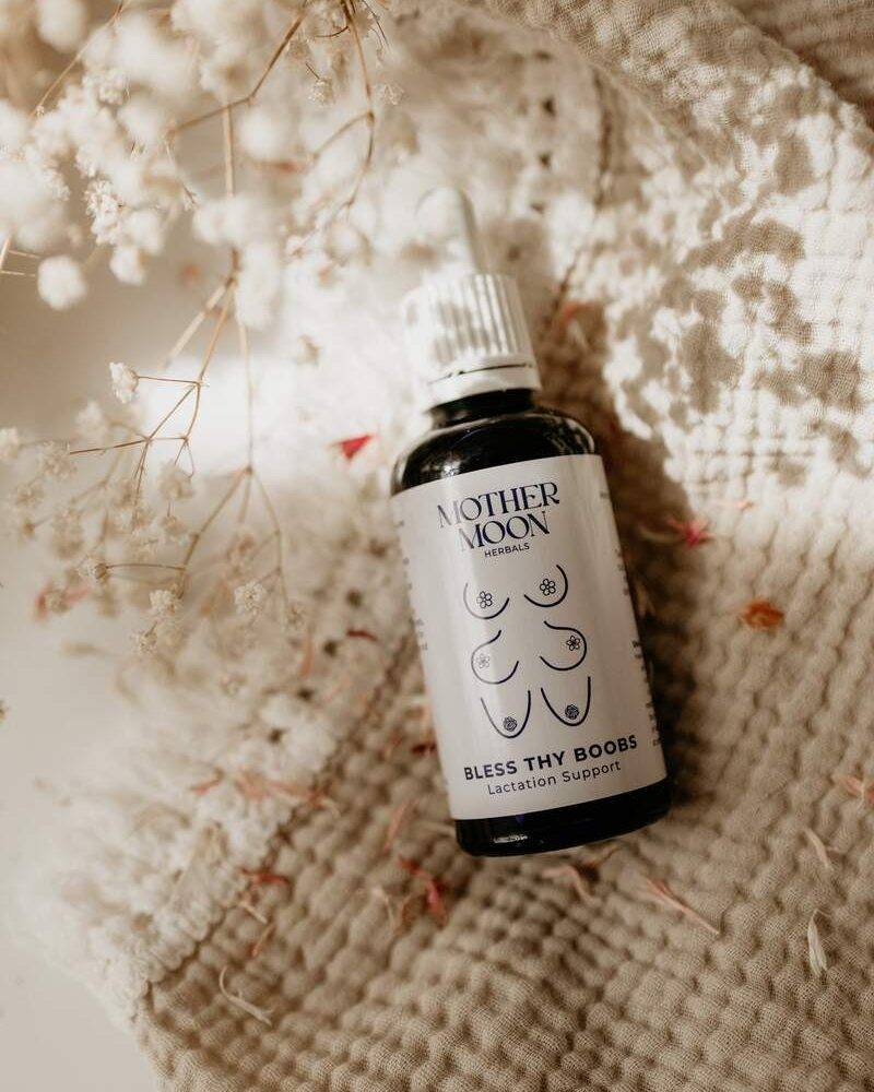 Mother Moon Bless Thy Boobs lactation support herbal tincture in a dark glass bottle with a dropper, surrounded by dried