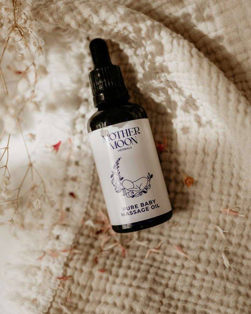 Mother Moon Pure Baby Massage Oil in a black glass bottle with a dropper, placed on a textured cream fabric.