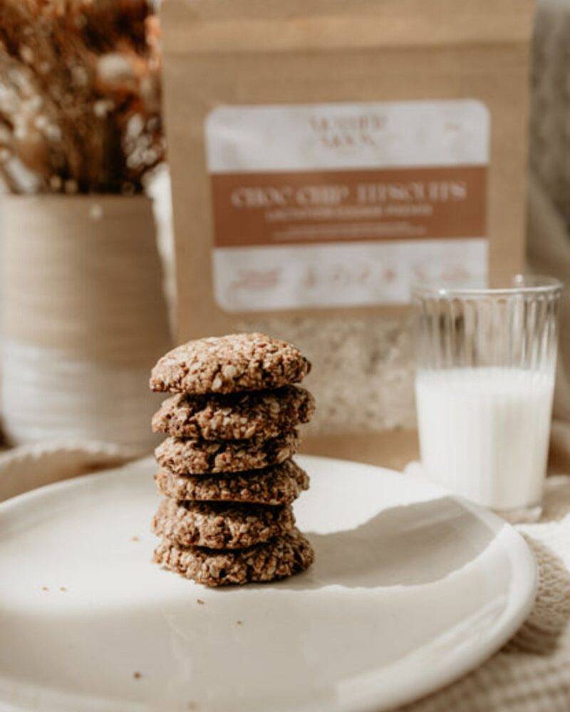 Lorna Jane choc chip biscuits stacked on a white plate with a glass of milk and decorative background.