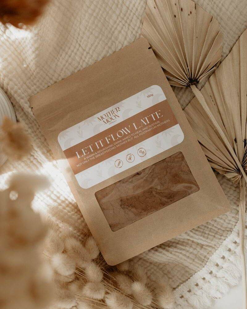 Mother Nourish Let It Flow Latte, 150g, in a kraft paper pouch with a floral label, surrounded by dried flowers and textured