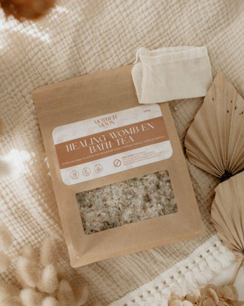 Healing Womb En Bath Tea by Nature's Nurture in a kraft paper pouch with a muslin bag, set on a textured blanket.