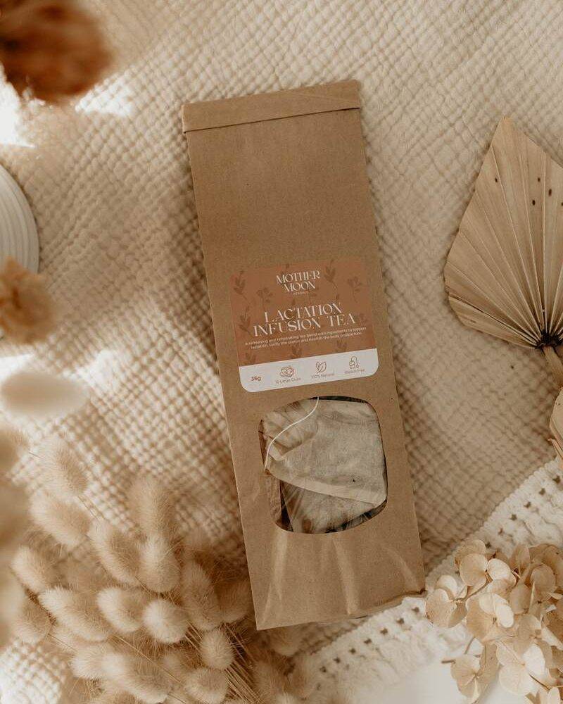 Lorna Jane Lactation Infusion Tea in a kraft paper bag with a clear window, placed on a textured beige fabric background.