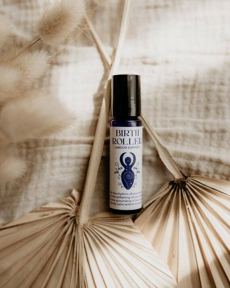 Lorna Jane Birth Roller for labour support in a blue bottle, placed on textured fabric with decorative dried leaves.