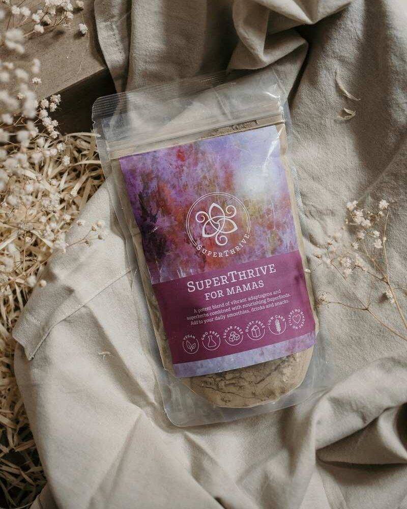 Superthrive for Mamas by Lorna Jane, packaged in a clear pouch with a colorful label, resting on soft fabric and dried
