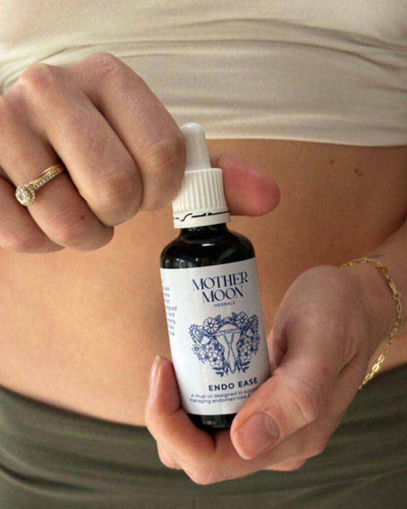 Mother Moon Endo Ease tincture in a dropper bottle held by a person, showcasing a minimalist design with a floral logo.